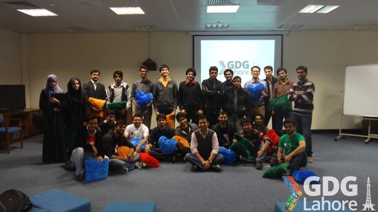 Large group photo at a GDG Lahore meetup, attendees seated and standing holding coloured cushions.