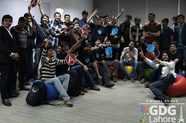 Attendees at a GDG Lahore session celebrating with raised hands, holding AngularJS and Firebase paper cut-outs.